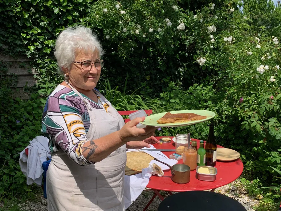 Eine Frau mit Schürze steht im Freien und reicht einen Teller mit Crepes