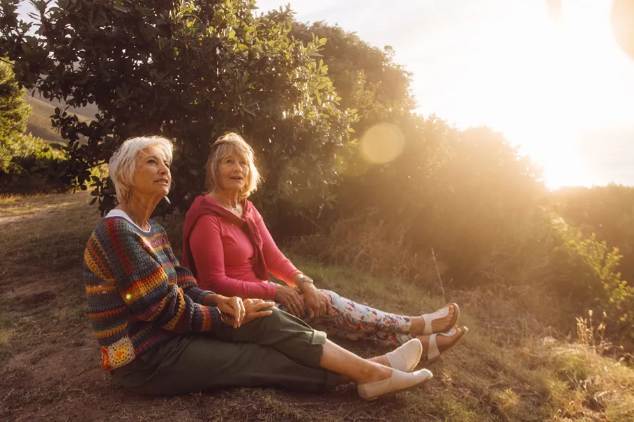 Zwei Frauen sitzen nebeneinander in der Natur, reden und schauen in den Himmel